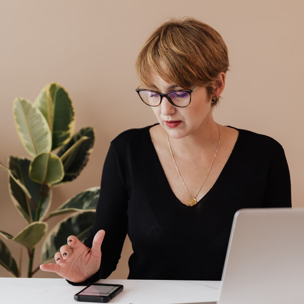 woman in front a computer and about to tap on her phone