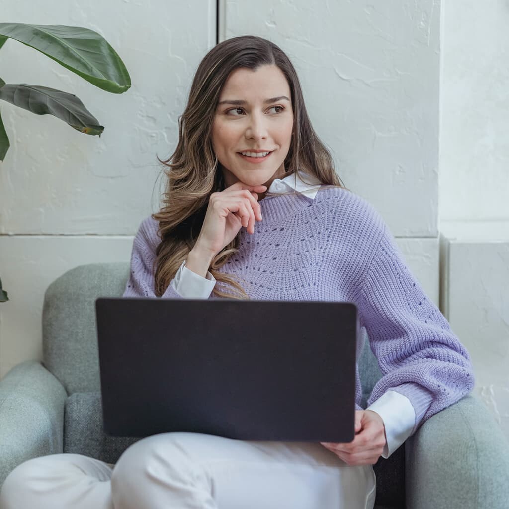 woman with a lilac sweater sitting with a laptop
